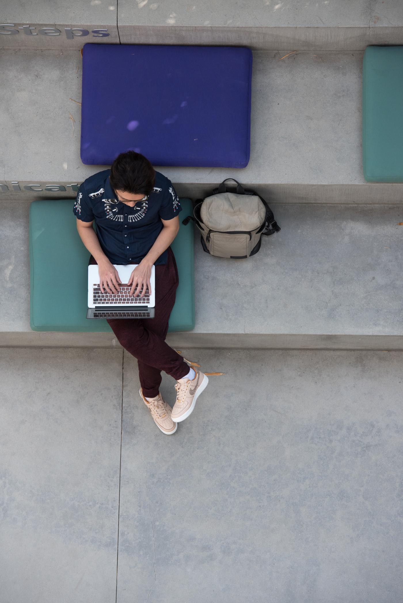 Person sitting on a cement bench on their laptop